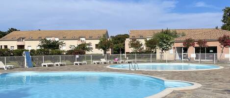 A swimming pool with a stone-tiled deck, lounge chairs, and a clear blue sky.