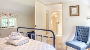 A bedroom with a bed, a chair, a window with curtains, a door, and a framed picture on the wall.