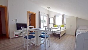 Une chambre avec un lit, un bureau et une chaise, une télévision et une fenêtre avec des rideaux.