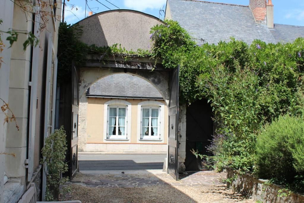 A narrow alleyway leading to a building with a stone archway, a small window, and a door.