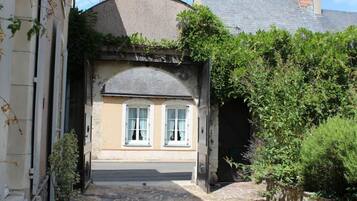 A narrow alleyway leading to a building with a stone archway, a small window, and a door.