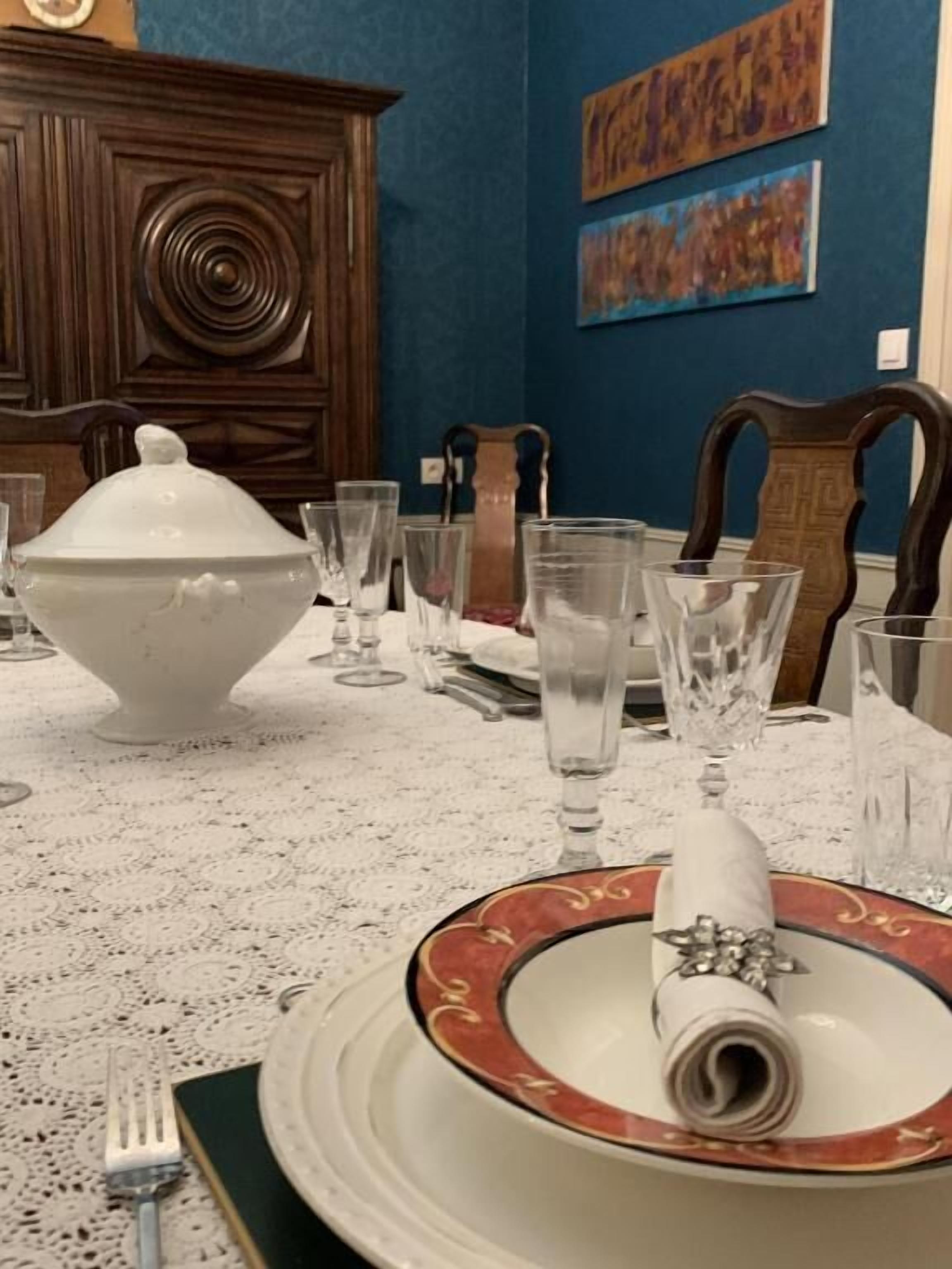 Een eettafel gedekt met een witte tafelkleed, een grote witte terrine en diverse glazen.