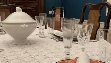 Een eettafel gedekt met een witte tafelkleed, een grote witte terrine en diverse glazen.