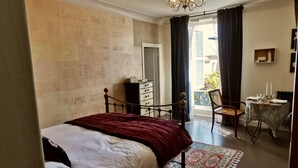 A bedroom with a bed, a dresser, a chair, a table with candles, and a view of the outside. - 5 Grande Rue (Le Lude)