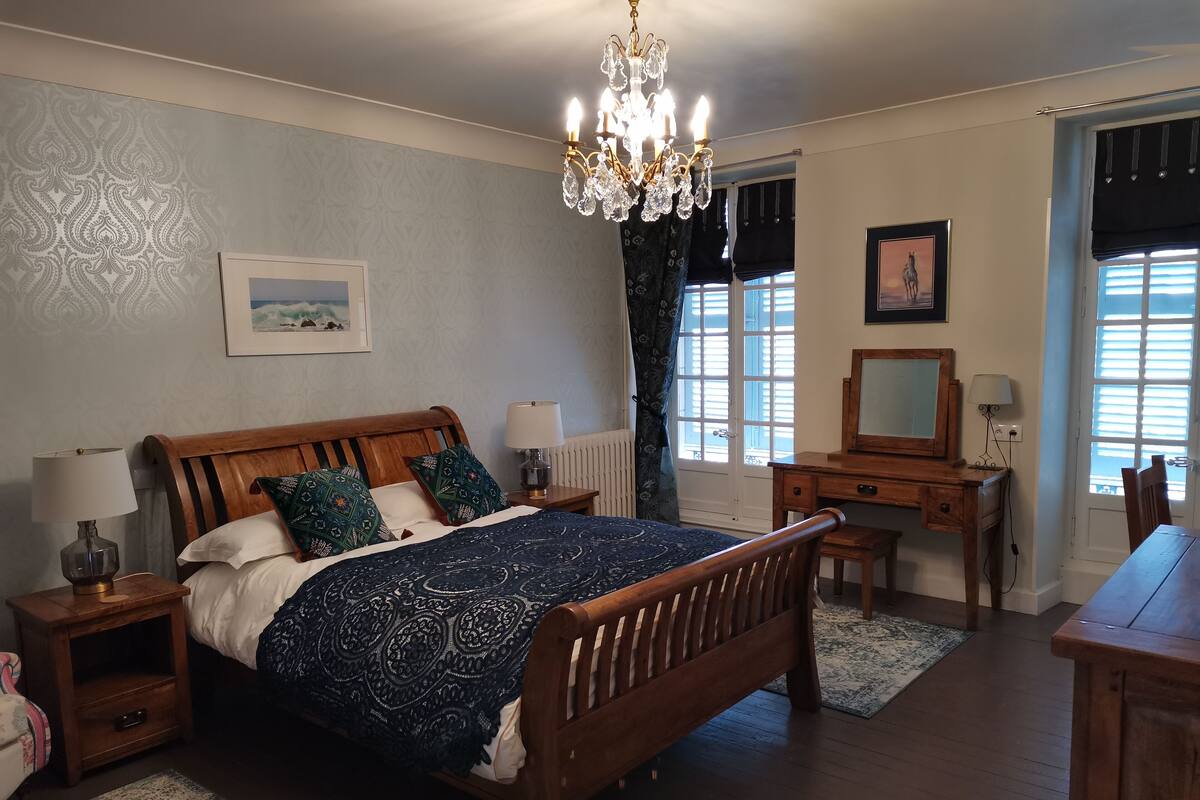 A bedroom with a wooden bed, nightstands, a dresser, a desk, and a chandelier.