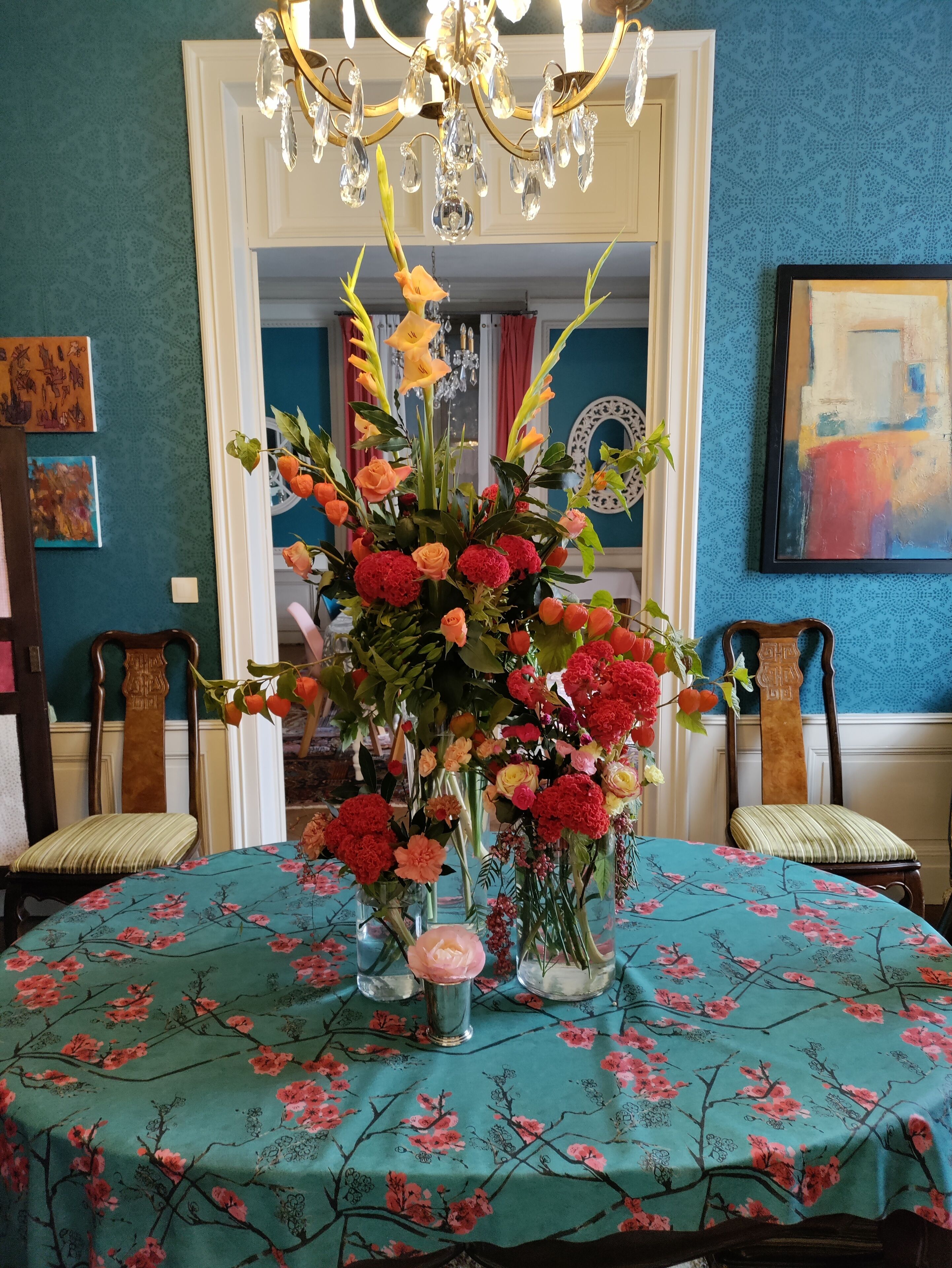 Una habitación con un mantel floral, una araña y un arreglo floral grande sobre la mesa.