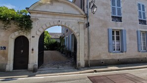 A historic building with an arched entrance, a street sign indicating '5 Rue', and a paved pathway leading to a gate. - 5 Grande Rue (Le Lude)