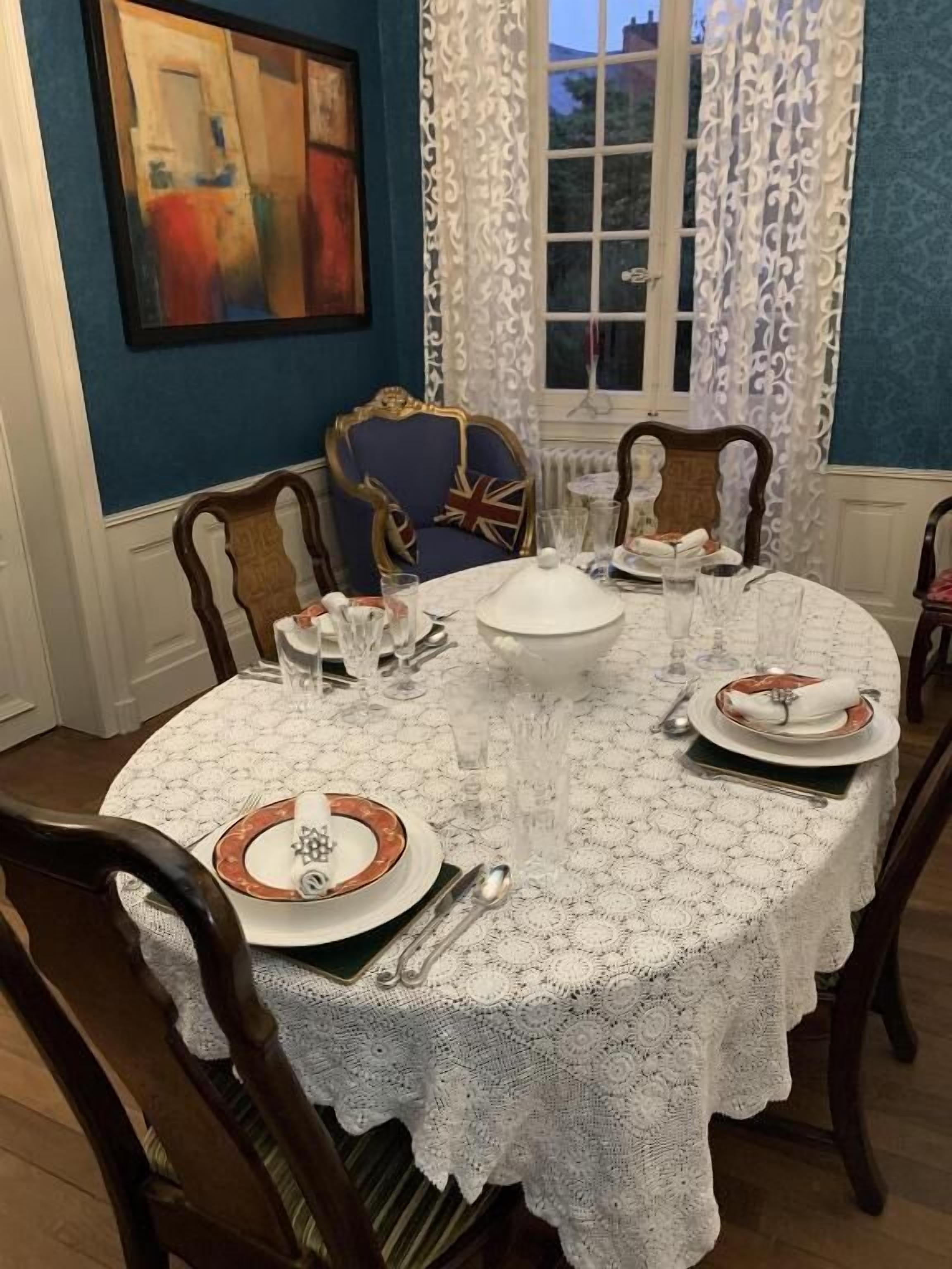 A dining table set with plates, glasses, and cutlery, surrounded by wooden chairs with a blue cushion.