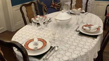 A dining table set with plates, glasses, and cutlery, surrounded by wooden chairs with a blue cushion.
