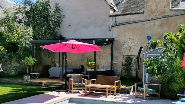 A swimming pool with a pink umbrella, outdoor furniture, and a stone wall in the background. - 5 Grande Rue (Le Lude)