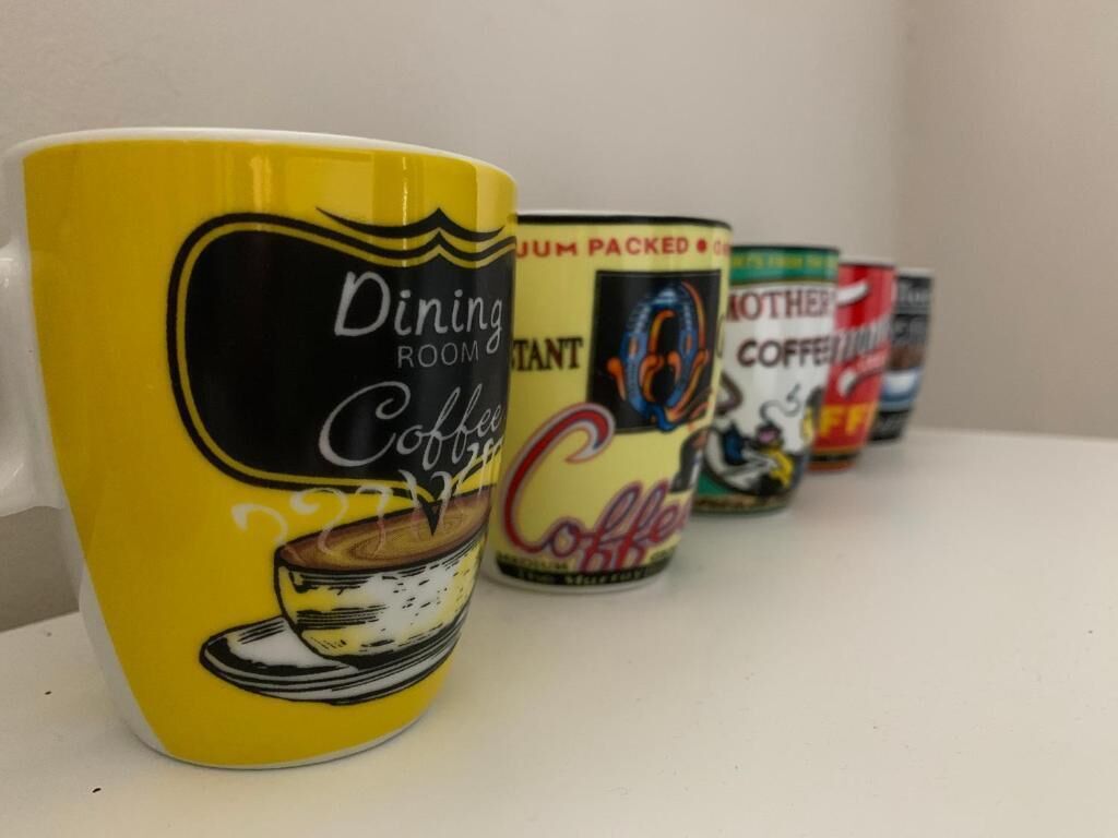 Eine Reihe von Kaffeetassen mit unterschiedlichen Designs auf einem Regal.