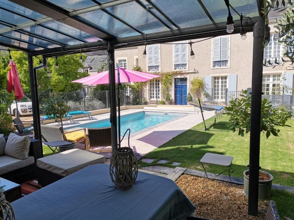 Un espacio al aire libre techado con piscina, sillas de descanso y una mesa con un florero.