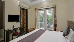 A hotel room with a bed, a desk with a chair, a television, an air conditioning unit, and a window with curtains. - Imperial Hotel Noida (Noida)