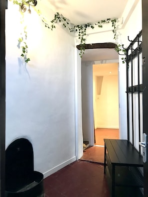 A narrow hallway with white walls, a black bench, and a door with a black metal handle. - Quintessentially charming in the heart of Grasse (Grasse)