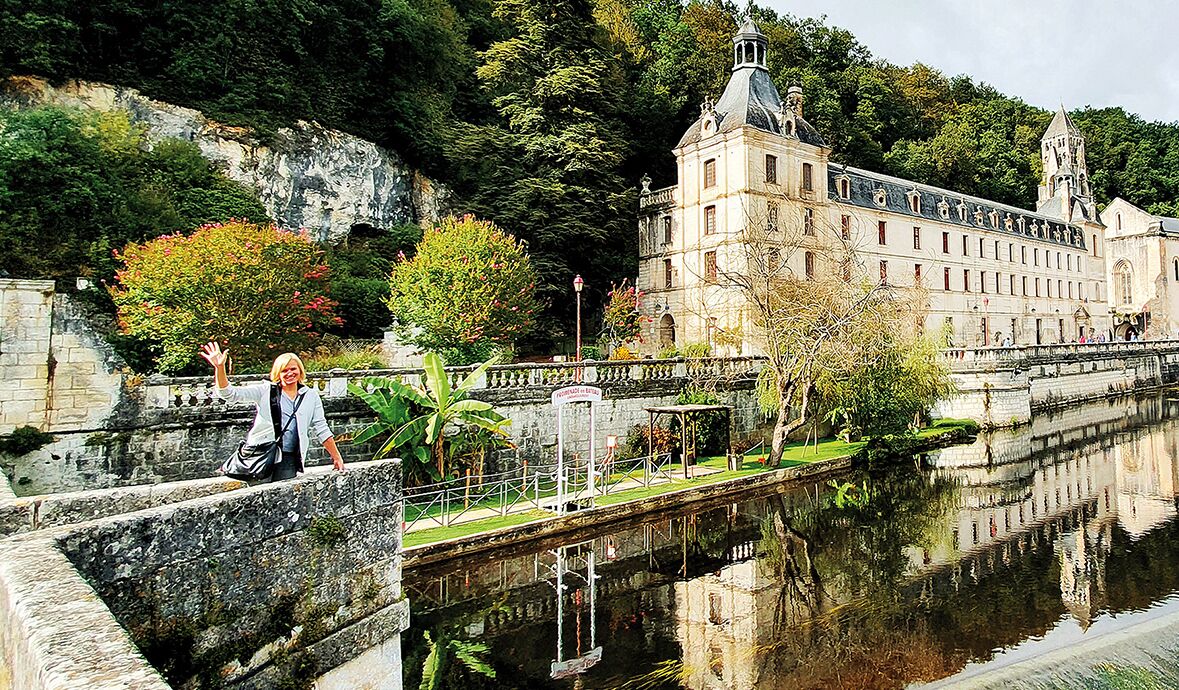 Un bâtiment historique doté d’une grande tour, d’un pont et d’une étendue d’eau paisible dans laquelle se reflète la structure.