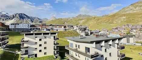 A modern multi-story building with balconies, surrounded by a mountainous landscape and other residential buildings.
