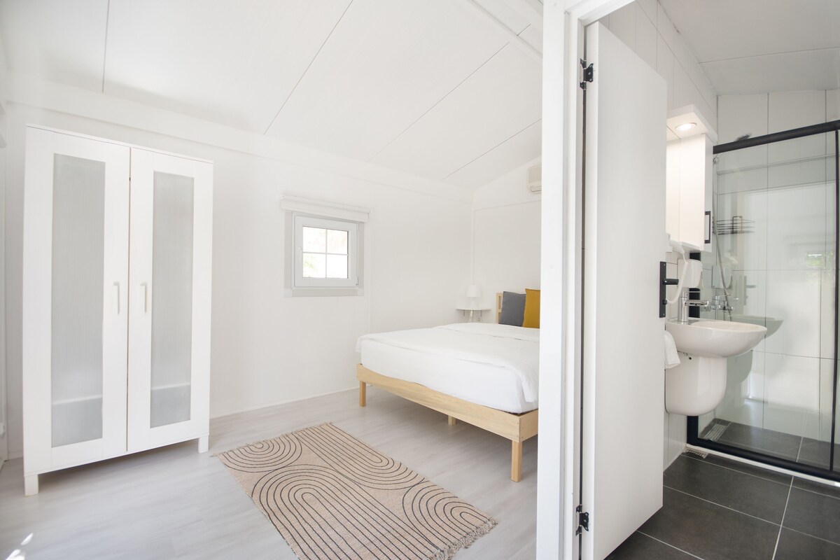 Une chambre à coucher comprenant un lit, une armoire, une fenêtre et une salle de bain avec un lavabo et une douche.