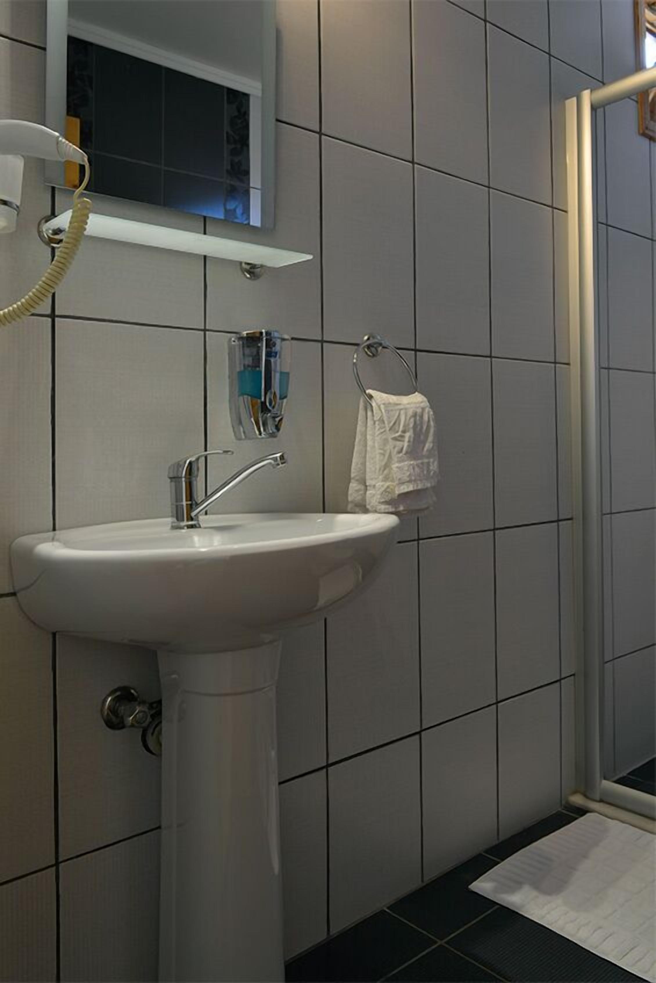 Un baño con lavamanos blanco, espejo y barra para toallas.