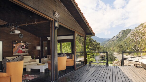 A wooden deck with a sofa and chairs, a dining table, and a view of a mountainous landscape. - Lukkies Lodge (Kemer)