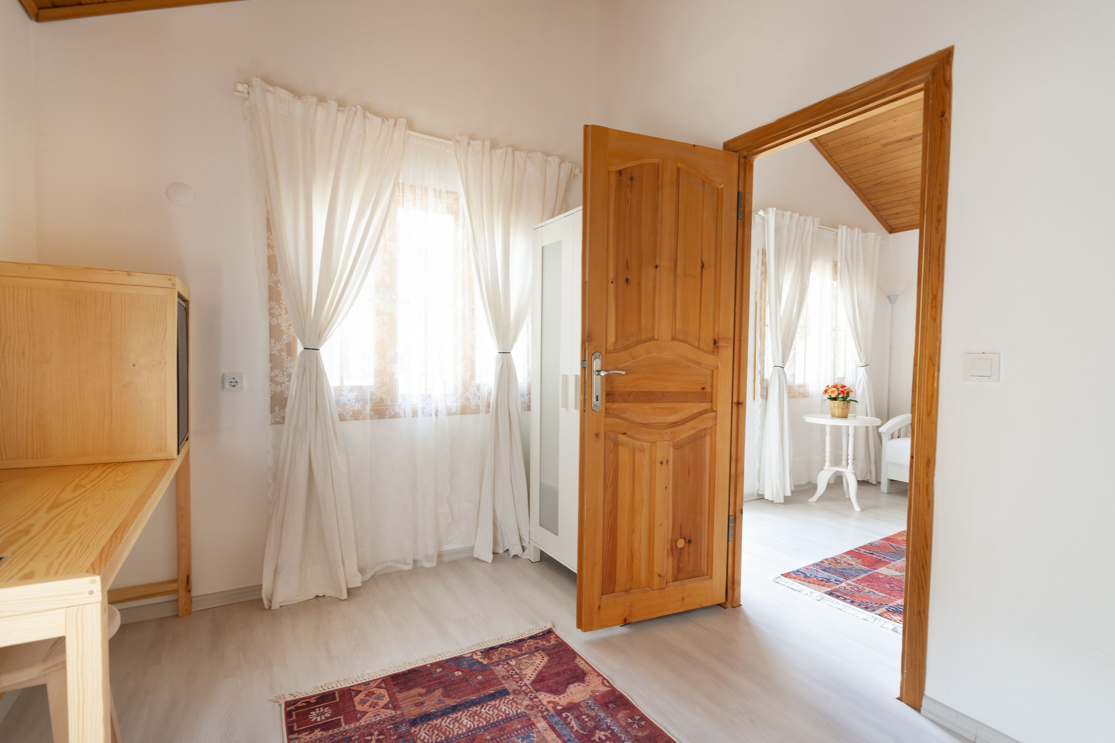 A room with a wooden door, a small table with a vase, and a patterned rug.