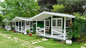 A row of small, white, single-story cottages with green walls and white roofs, each with a porch and potted plants. - Lukkies Lodge (Kemer)