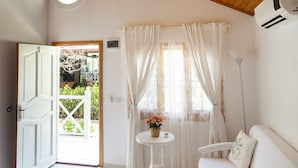 A room with a wooden ceiling, a white sofa, a small round table with a plant, and a view through a door to an outdoor area. - Lukkies Lodge (Kemer)
