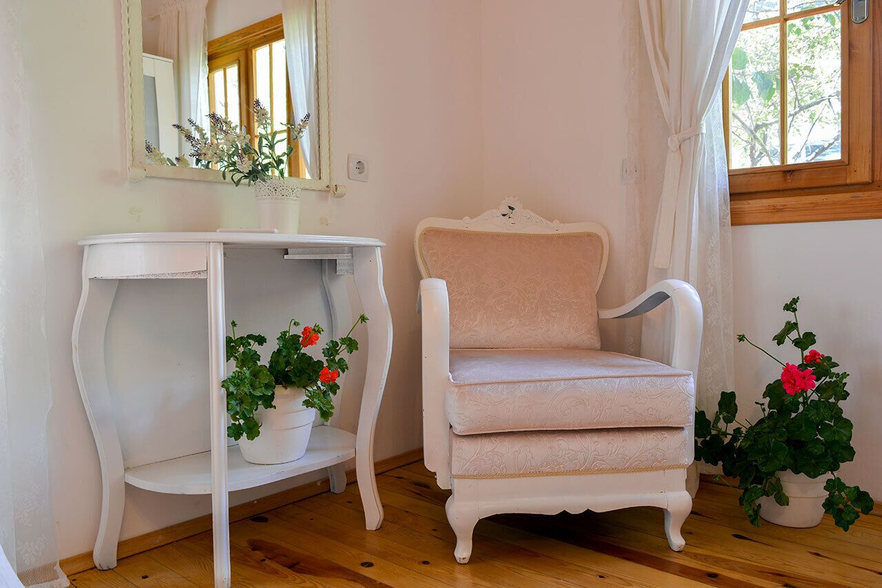 Ein Zimmer mit einem weißen Schminktisch, einem weißen Stuhl und zwei Blumentöpfen mit Blumen.