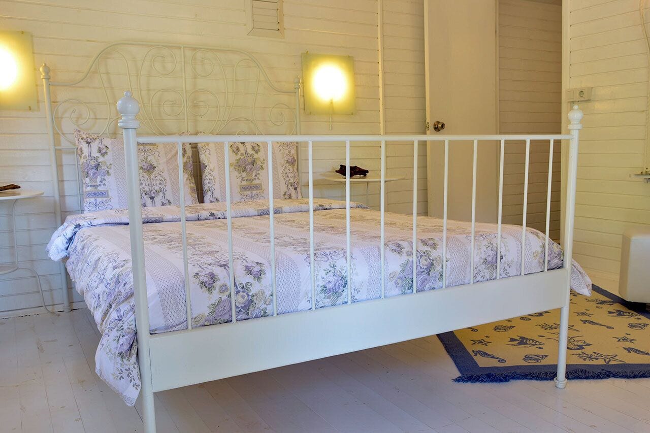 A white metal bed with floral bedding, a bedside table, and a nightstand.