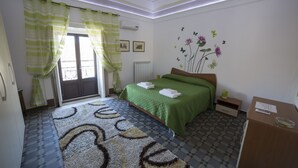 A hotel room with a bed, a small bedside table, a radiator, a window with curtains, and a wall with a floral mural. - CASA GRANDE ALCALA HISTORIC CENTER (Catania)