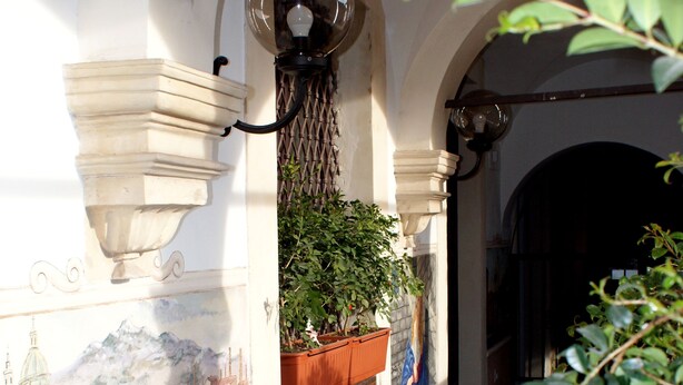 A narrow corridor with a tiled mural of a bridge and water, potted plants, and a staircase. - CASA GRANDE ALCALA HISTORIC CENTER (Catania)