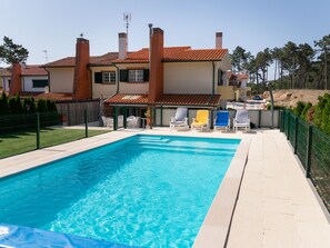 Ein Swimmingpool mit Liegestühlen, eine umzäunte Terrasse und ein Haus mit einem Ziegeldach.