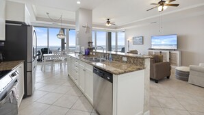 Una cocina moderna con una isla central, muebles blancos y un amplio ventanal con vista al océano.