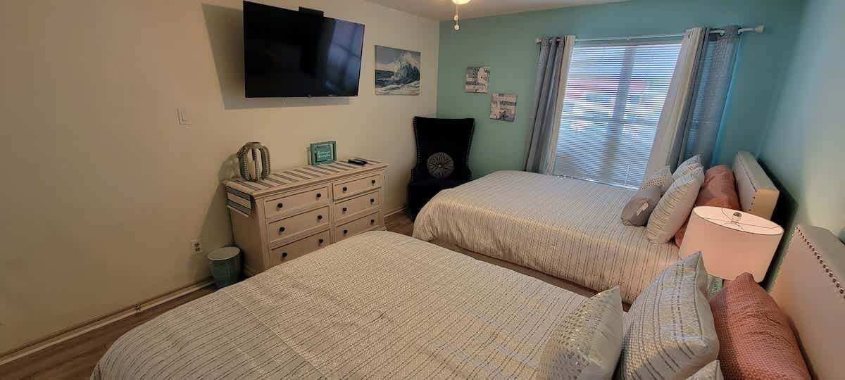 Un dormitorio con dos camas, un aparador, un televisor y una ventana con cortinas.