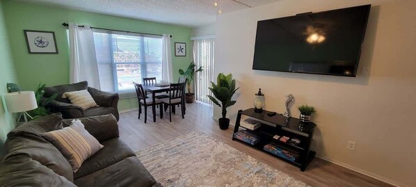 A living room with a sofa, a dining table, chairs, a TV, and a bookshelf.