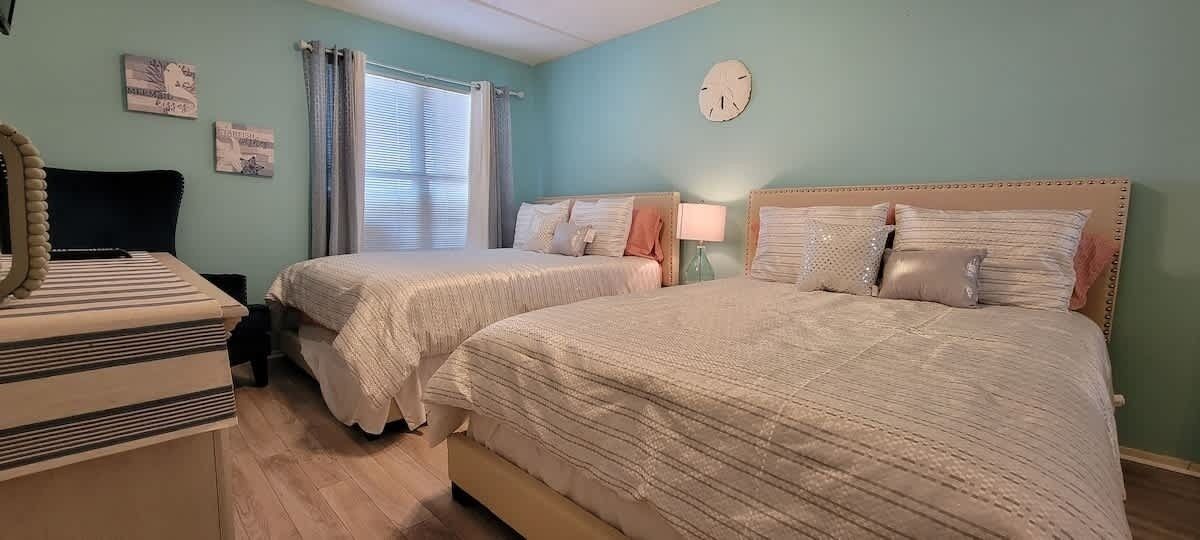 A bedroom with two beds, a dresser, a mirror, and a window with curtains.