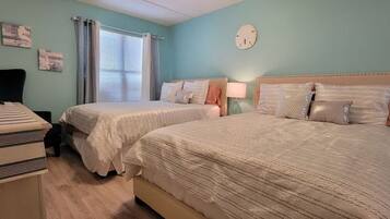 A bedroom with two beds, a dresser, a mirror, and a window with curtains.