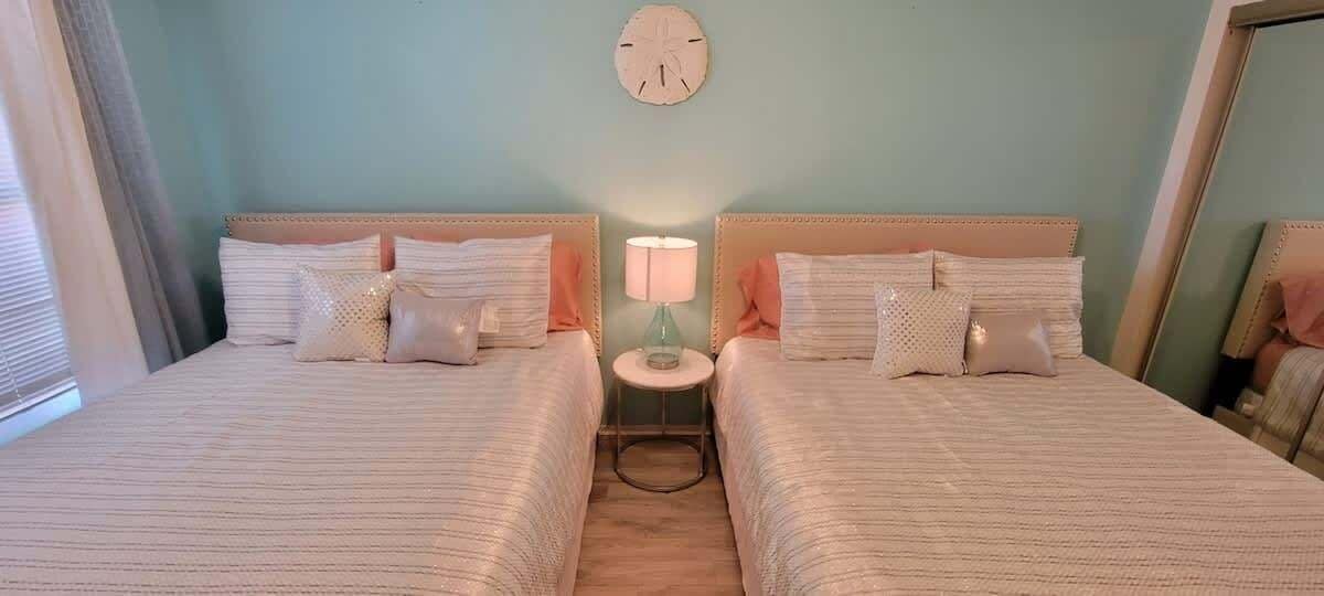 Une chambre avec deux lits, une horloge murale ronde et une petite table avec une lampe placée entre les lits.