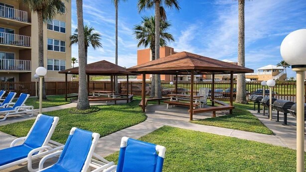 A poolside area with lounge chairs, wooden gazebos, and palm trees. - Private Beach Access Pool & Hot Tub Bbq Pits 1 Bedroom Home by RedAwning (South Padre Island)
