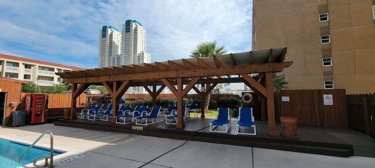 A pool area with a wooden pergola, lounge chairs, and a Coca-Cola vending machine.