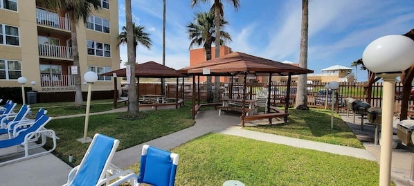 Un patio con mesas al aire libre, palmeras y un edificio al fondo.