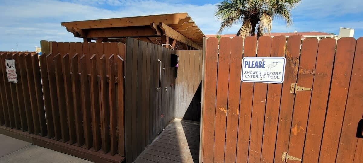 A wooden gate with a sign instructing to shower before entering the pool area.