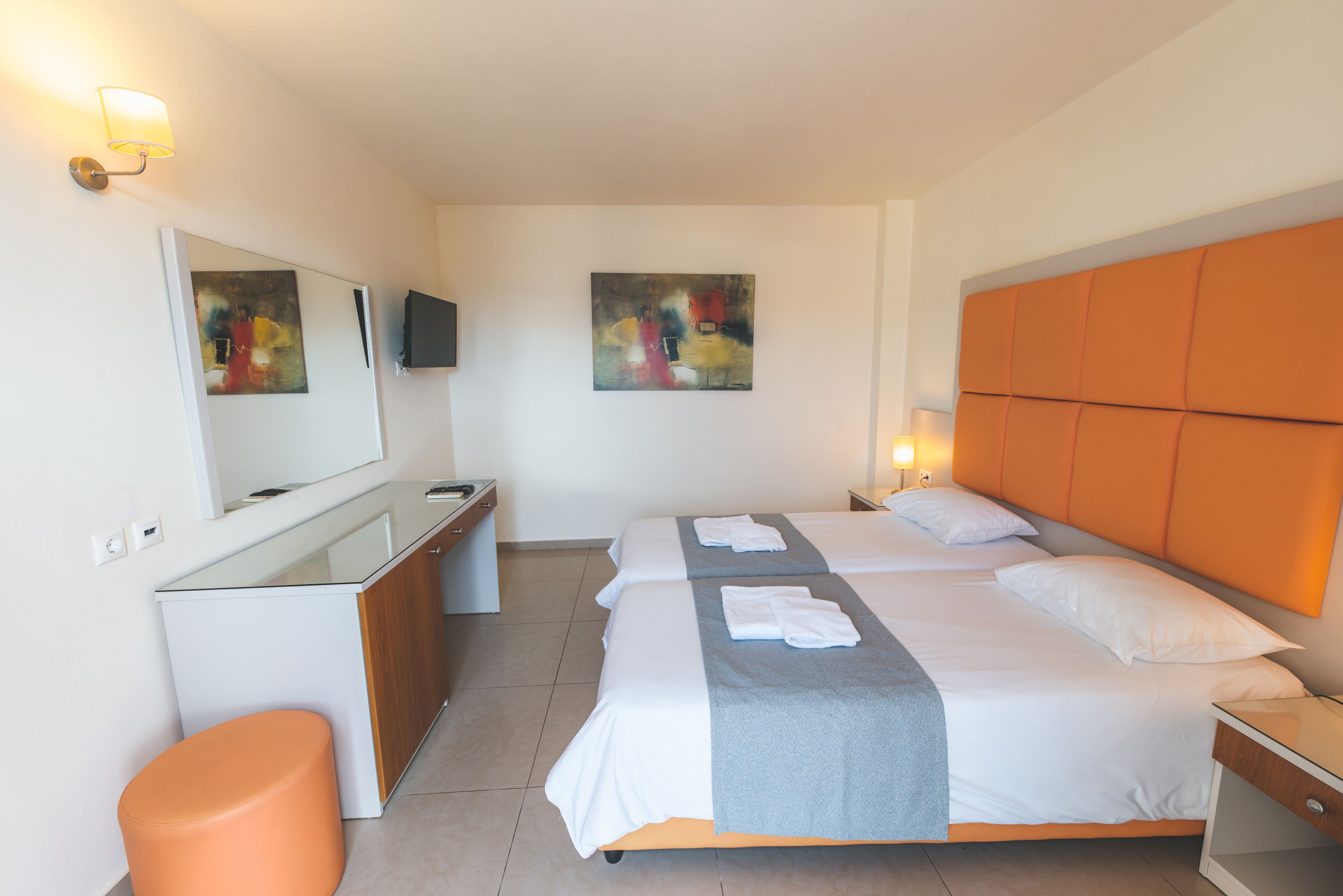 A hotel room with two beds, a desk, a chair, and artwork on the walls.