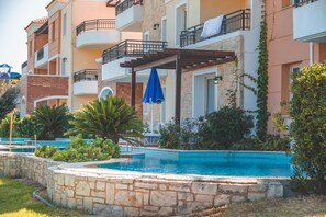 Zona de piscina con muros de piedra, una pérgola y una sombrilla azul.