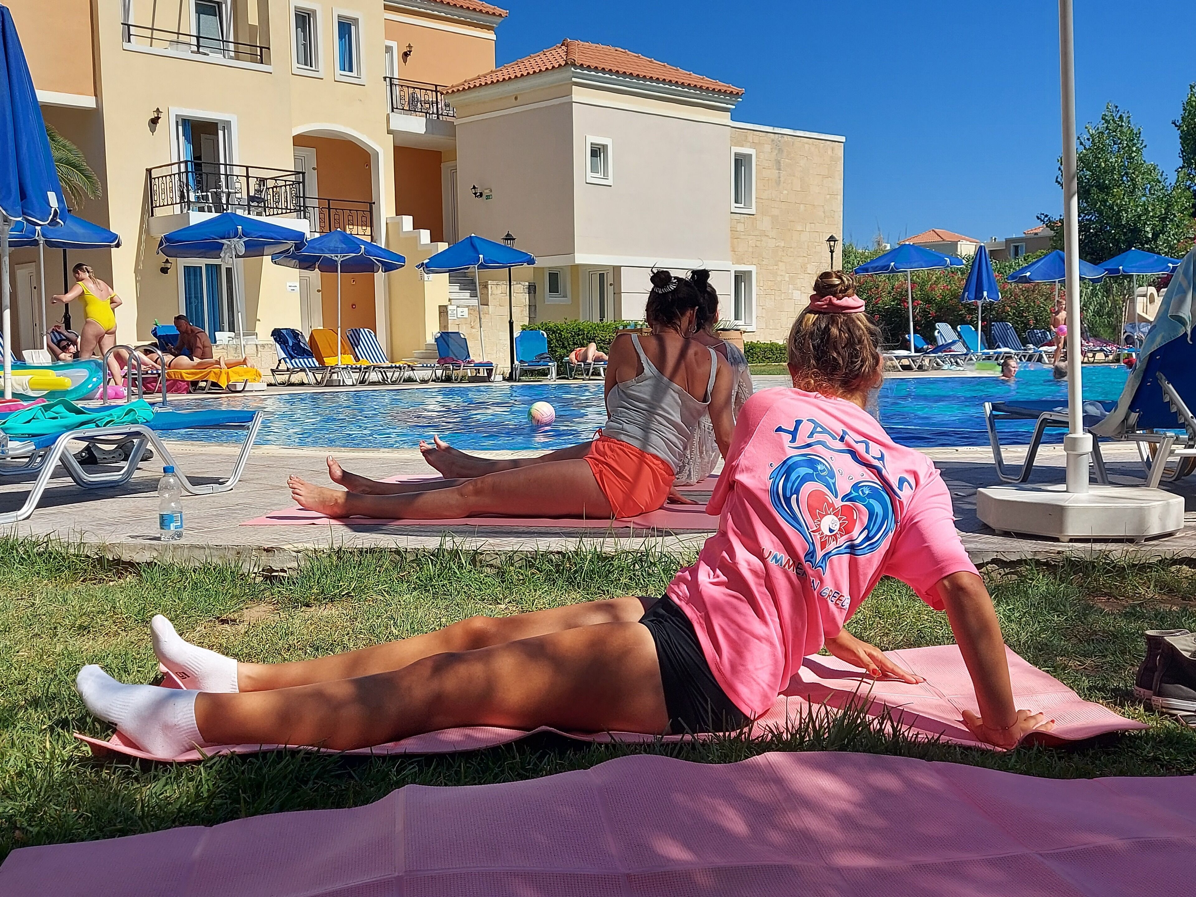 Un área junto a la piscina con sillones de descanso y sombrillas, una piscina y un edificio con balcones.