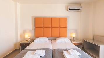 A hotel room with two beds, a headboard, bedside tables with lamps, and an air conditioning unit.