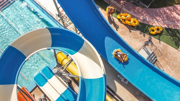 Un parc aquatique doté d’un grand toboggan bleu et blanc, de bouées jaunes et d’une zone de piscine.