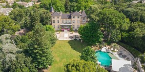 A large, multi-story house with a swimming pool surrounded by lush greenery.