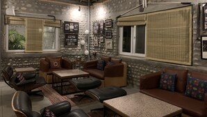 A cozy living room with a stone wall, a wooden ceiling, and a large window with a view. - Anand at the Satluj (Anandpur Sahib)
