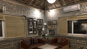 A cozy living room with a stone wall, framed pictures, a wooden ceiling, and a window. - Anand at the Satluj (Anandpur Sahib)