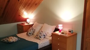 A small, cozy bedroom with a sloped ceiling, a single bed with patterned bedding, two bedside tables with lamps, and a wooden wardrobe. - Gîte in the heart of a vineyard. (Razac-de-Saussignac)